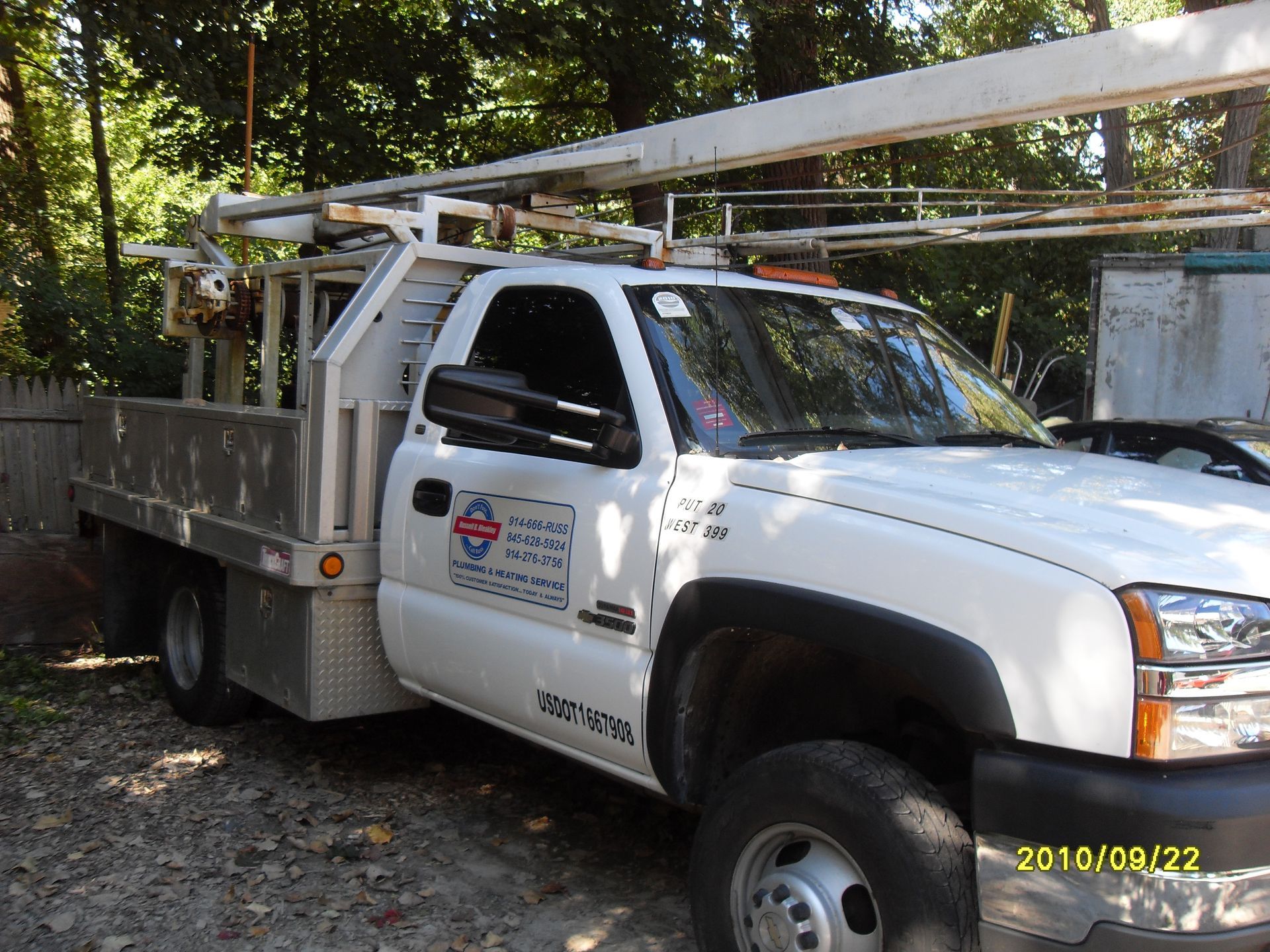 White work truck with a flatbed and ladder rack parked outside, featuring business logo on the door.