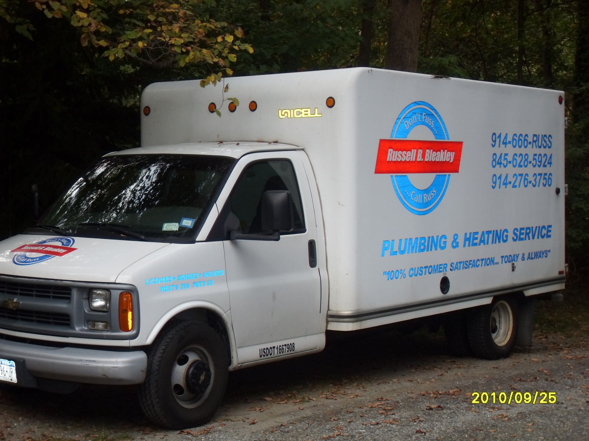 White plumbing service truck parked outdoors, with company logo and phone numbers.