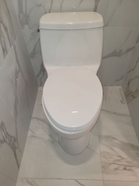 A white toilet is sitting on a tiled floor in a bathroom.