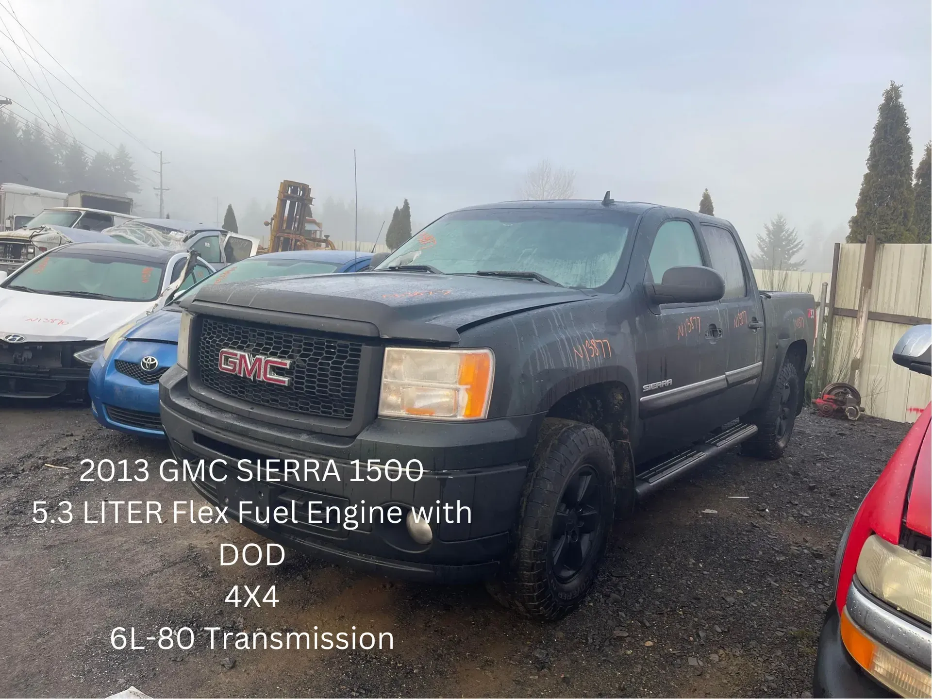 2013 black GMC Sierra truck with 6.3L engine, 4x4, at a junkyard on an overcast day.