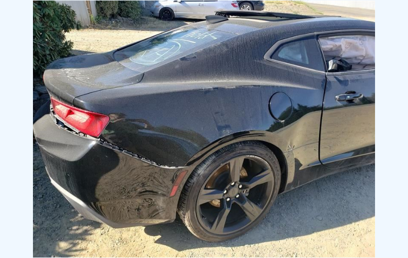 Black Chevrolet Camaro with rear damage parked outside.