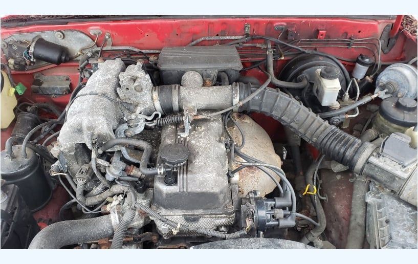 Red engine bay with a dusty engine and various components, hoses, and wiring.