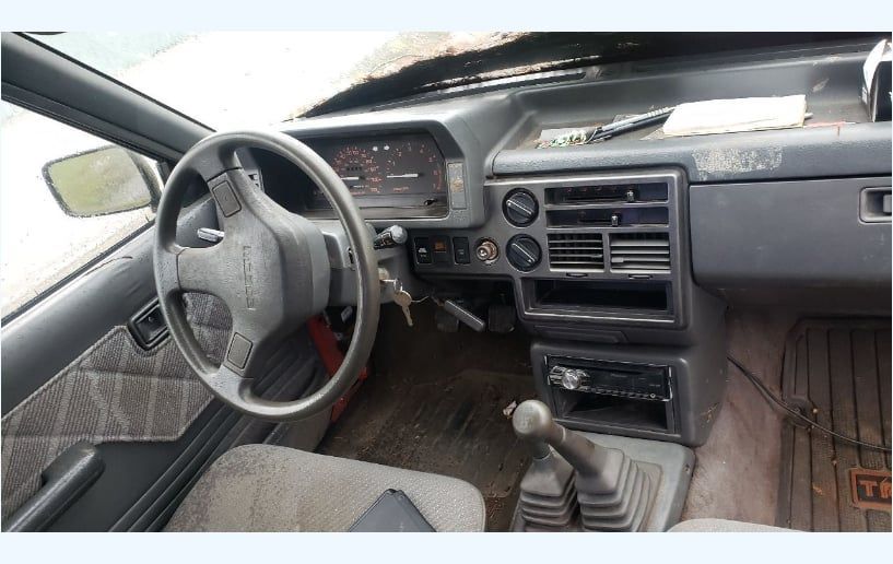 Interior of a gray car dashboard with steering wheel, gauges, radio, and gear shift.
