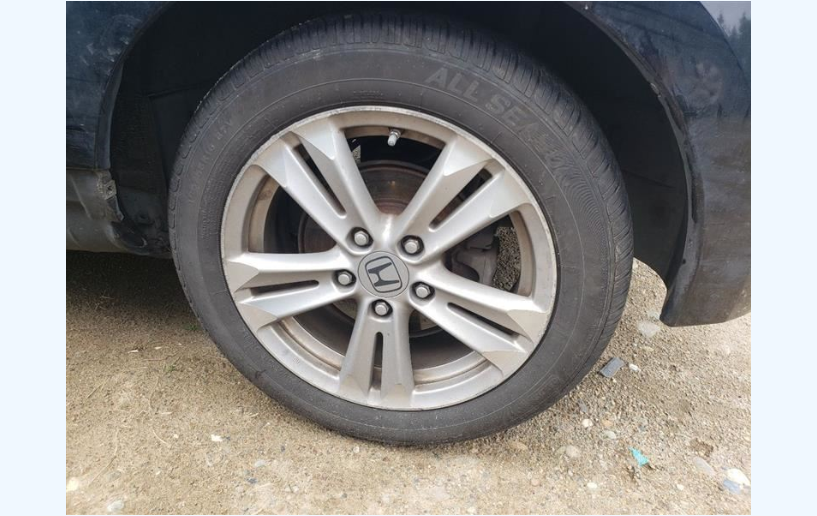 Black car wheel with silver rim, tire on a dirty surface.