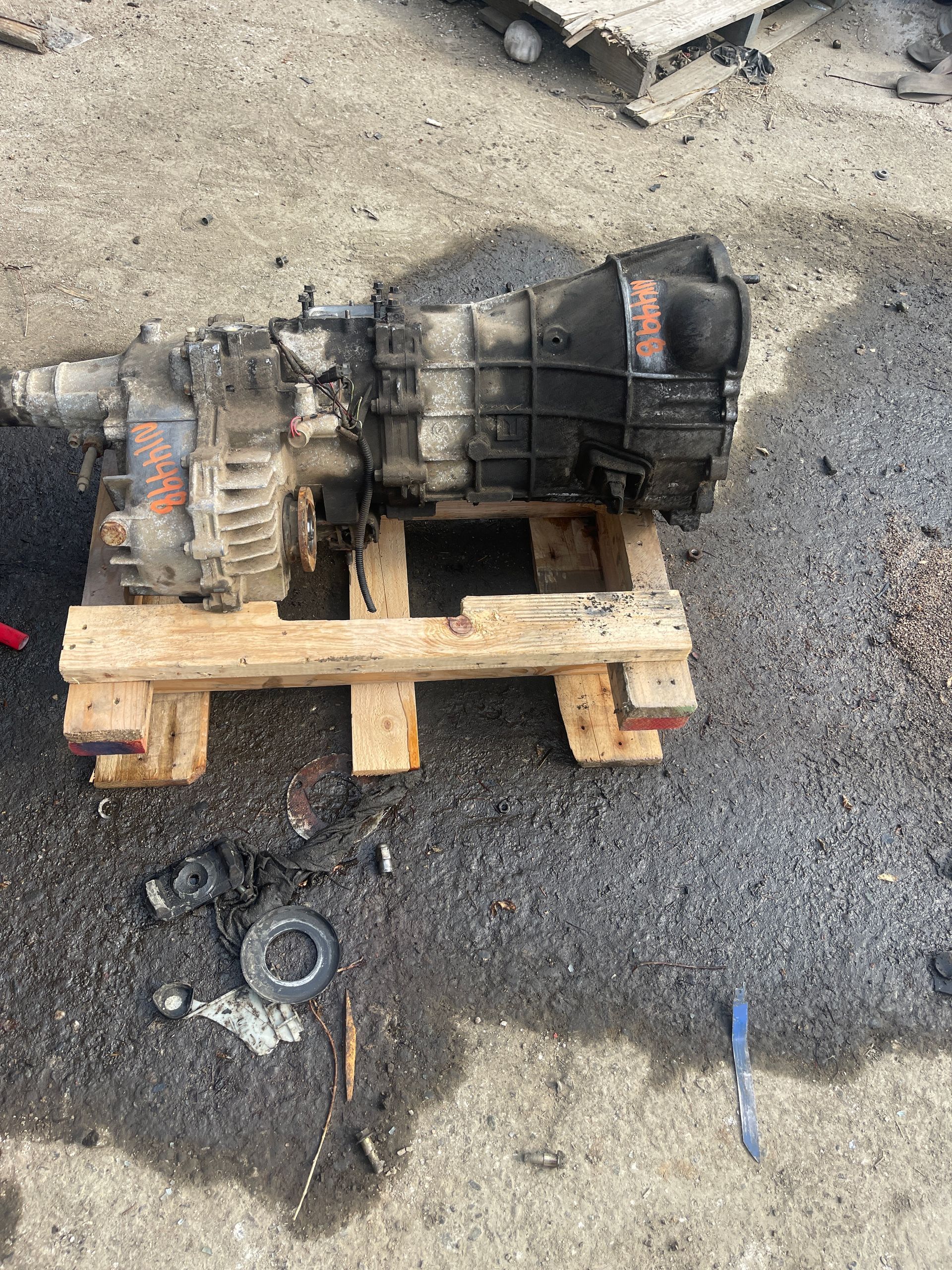 Dirty transmission on a wooden pallet, resting on a gravel surface. Parts scattered around.