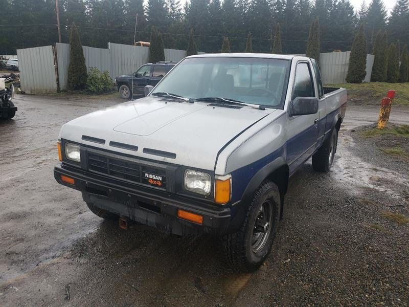 Silver and blue Nissan pickup truck parked outdoors on wet ground.