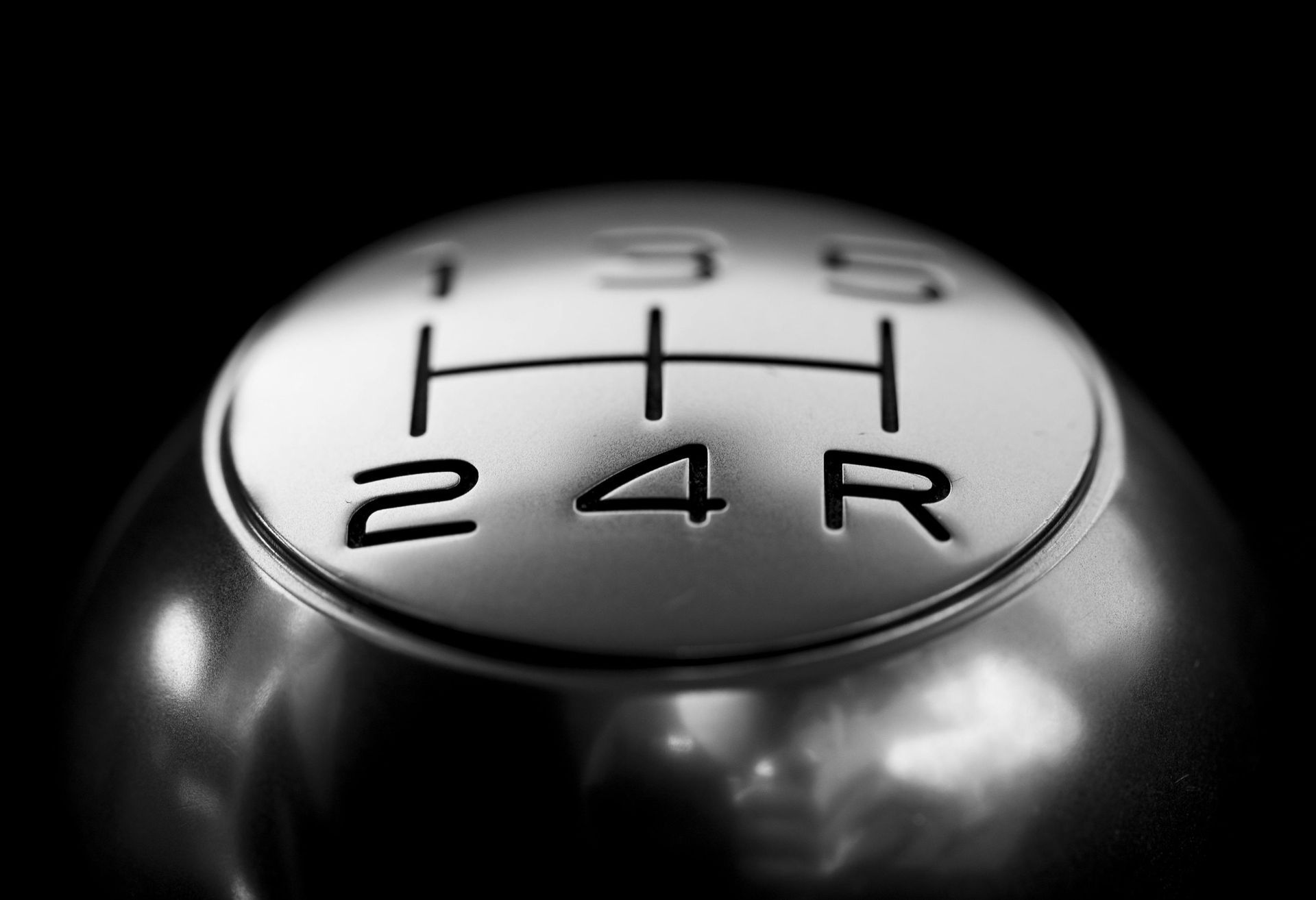 Close-up of a silver gear shift knob with numbers 1-5 and R (reverse) on a black background.