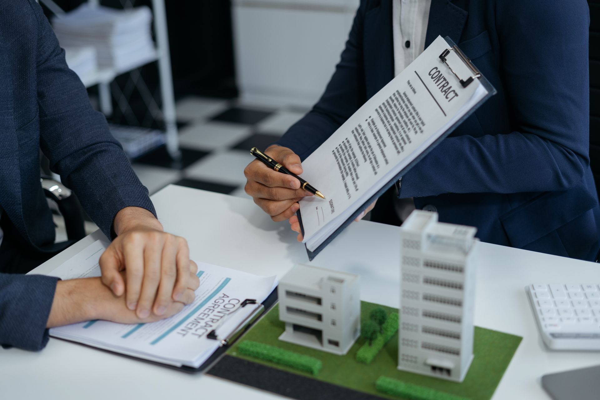 A man and a woman are sitting at a table with a model of a building and a clipboard.