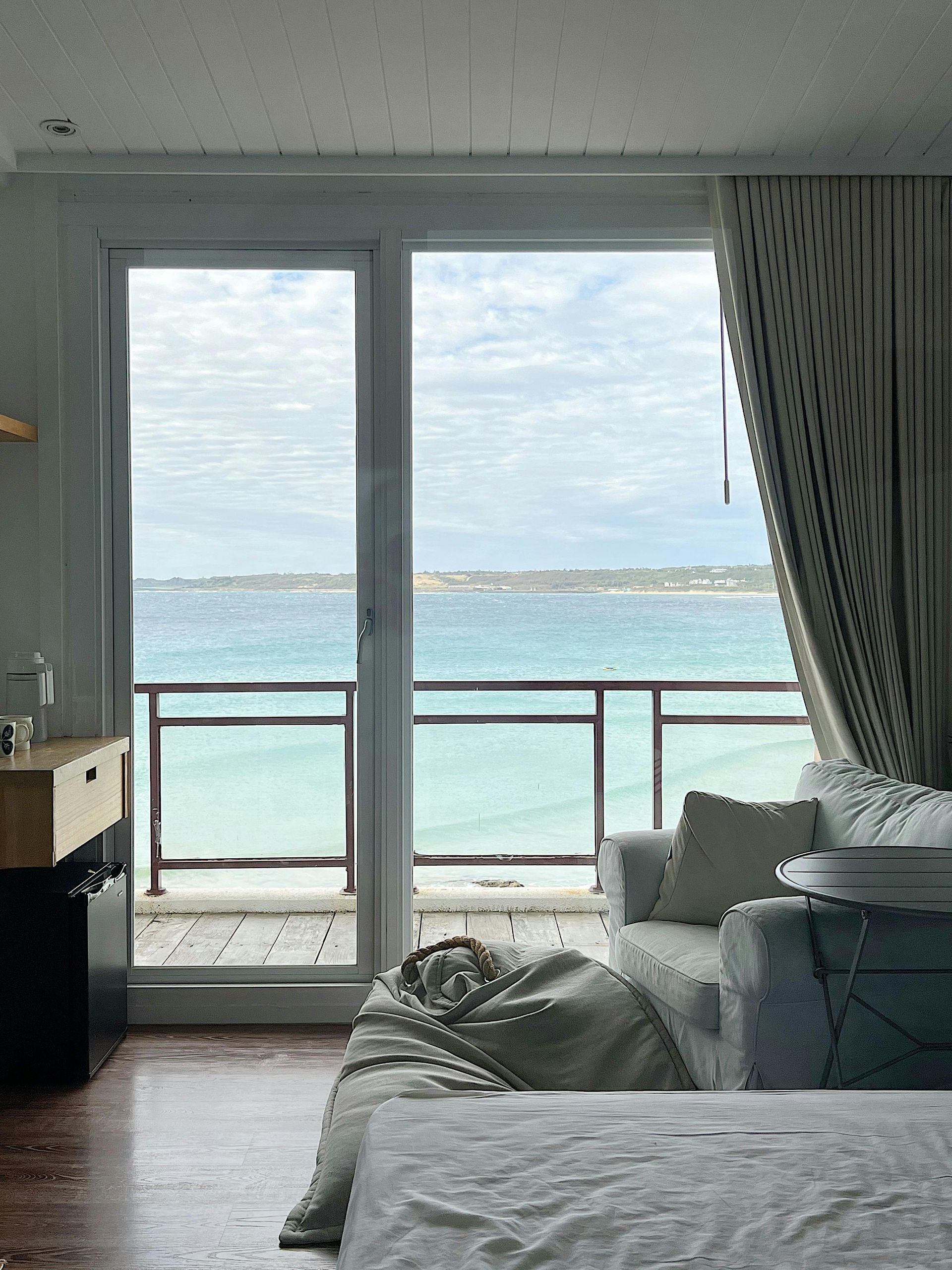 A bedroom with a bed , couch , and balcony overlooking the ocean.
