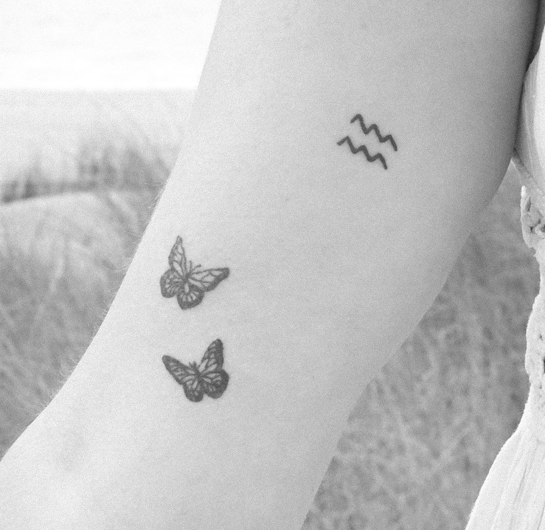 A black and white photo of a woman 's arm with a tattoo of butterflies and a zodiac sign.