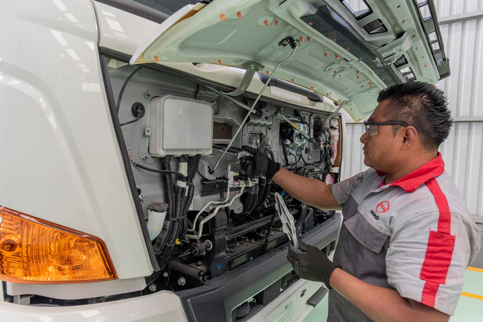 Mecânico de macacão vermelho e cinza, trabalhando em um caminhão branco em uma oficina.