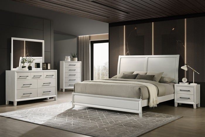 A modern white bedroom set with a bed, dresser with mirror, chest of drawers, and nightstand on a patterned area rug.