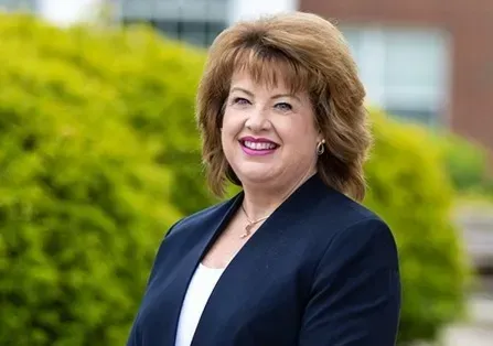 A woman in a blue jacket and white shirt is smiling for the camera.