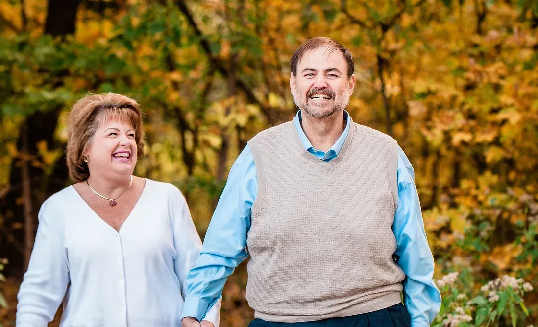 A man and a woman are holding hands while walking in the woods.