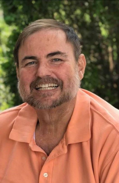 A man with a beard is wearing an orange shirt and smiling.