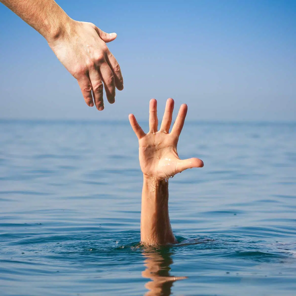 A person is reaching out to help another person who is drowning in the ocean.