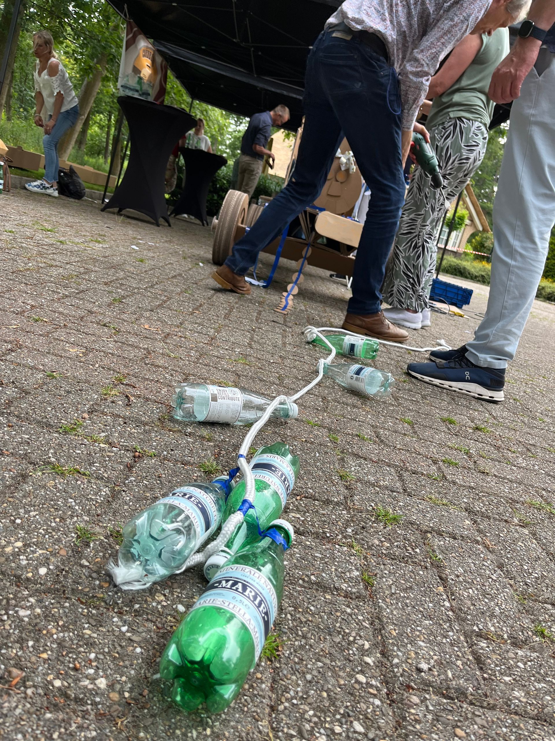 Een groep mensen staat rond een stapel plastic flessen op de grond.