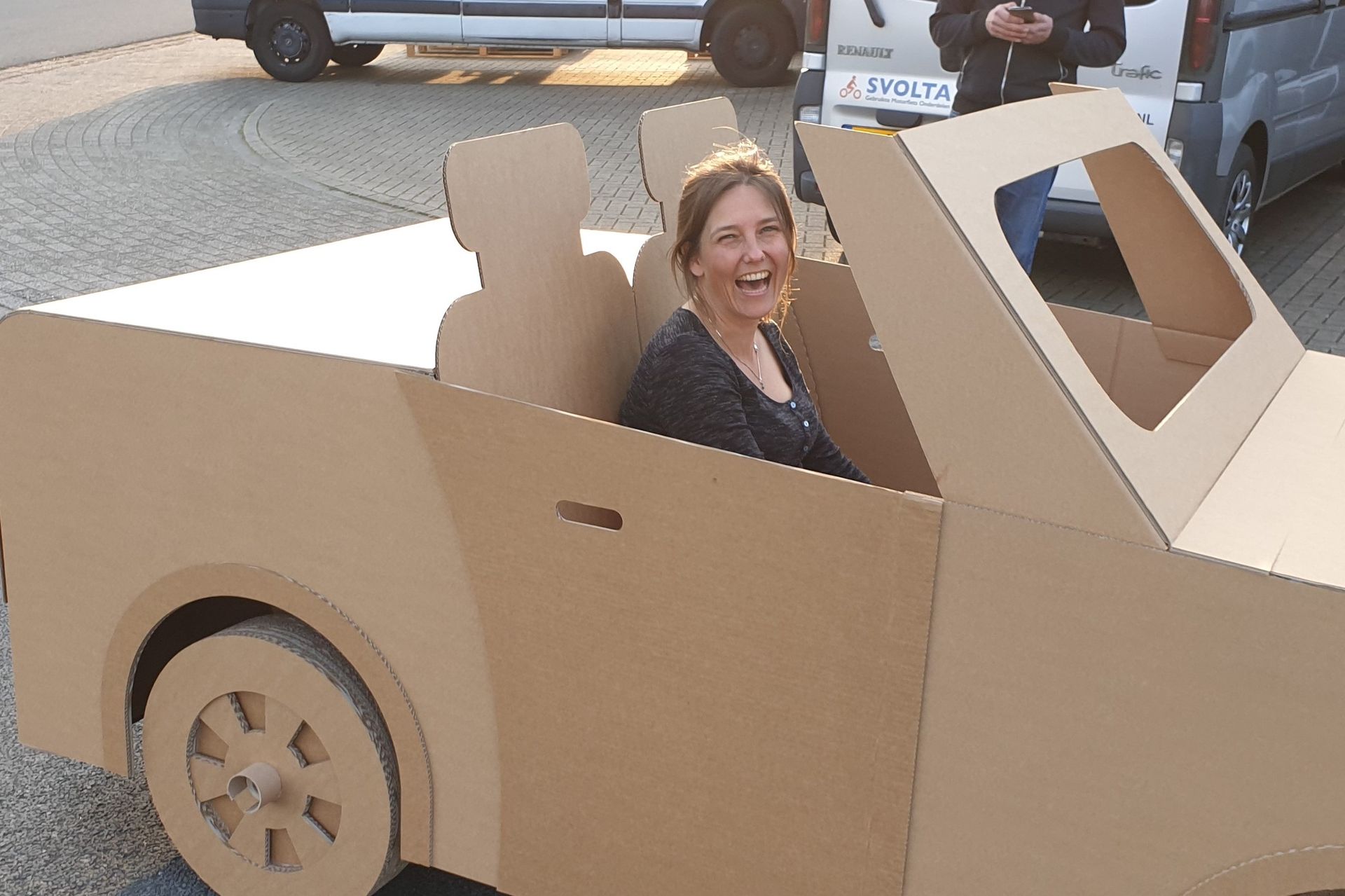 Een vrouw zit in een kartonnen auto