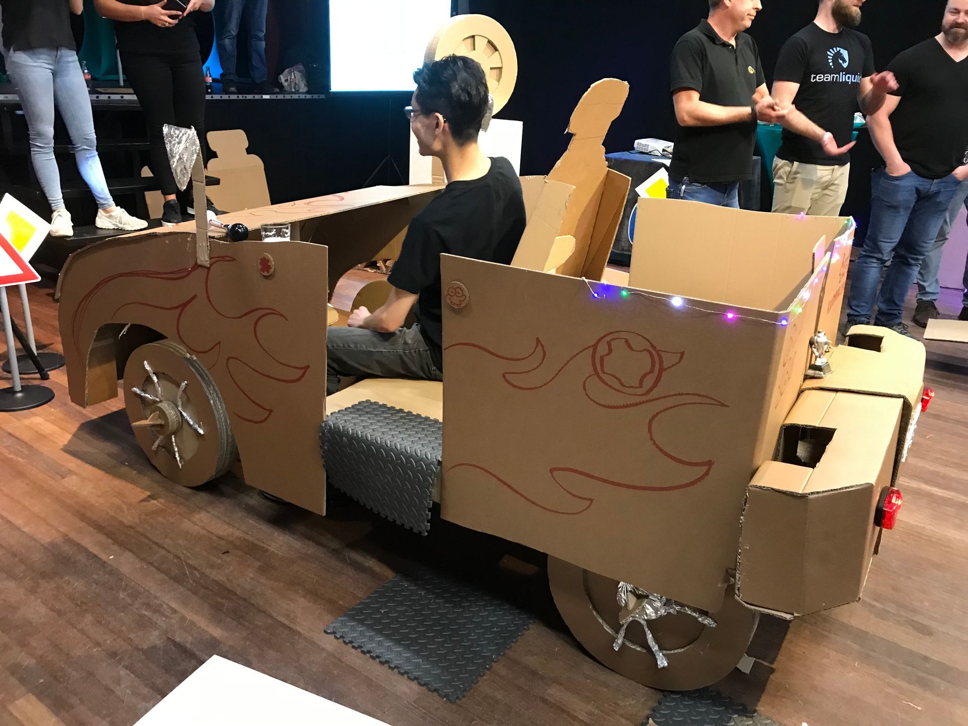 Een man zit in een kartonnen auto.