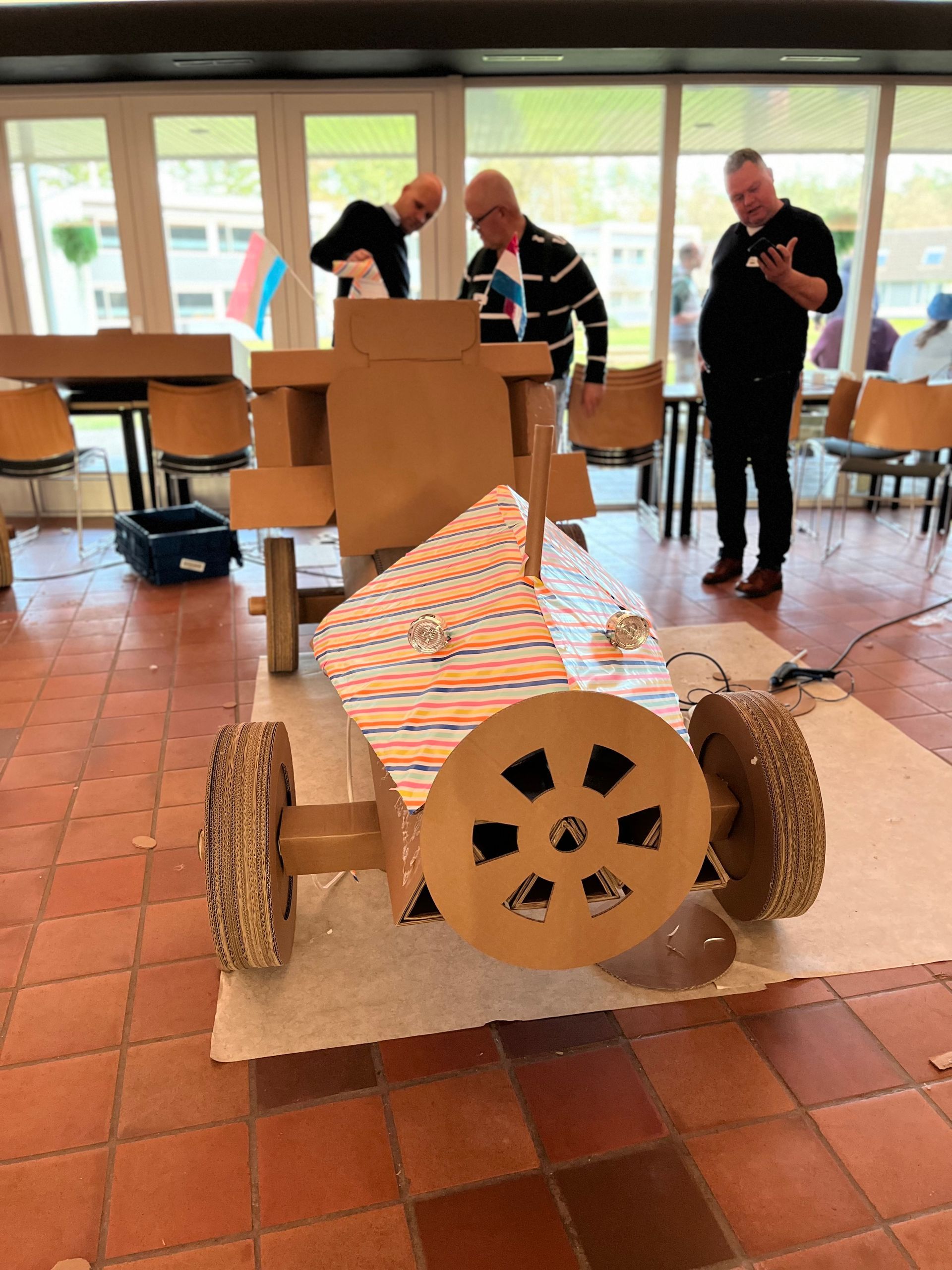 Twee mannen werken in een kamer aan een kartonnen auto