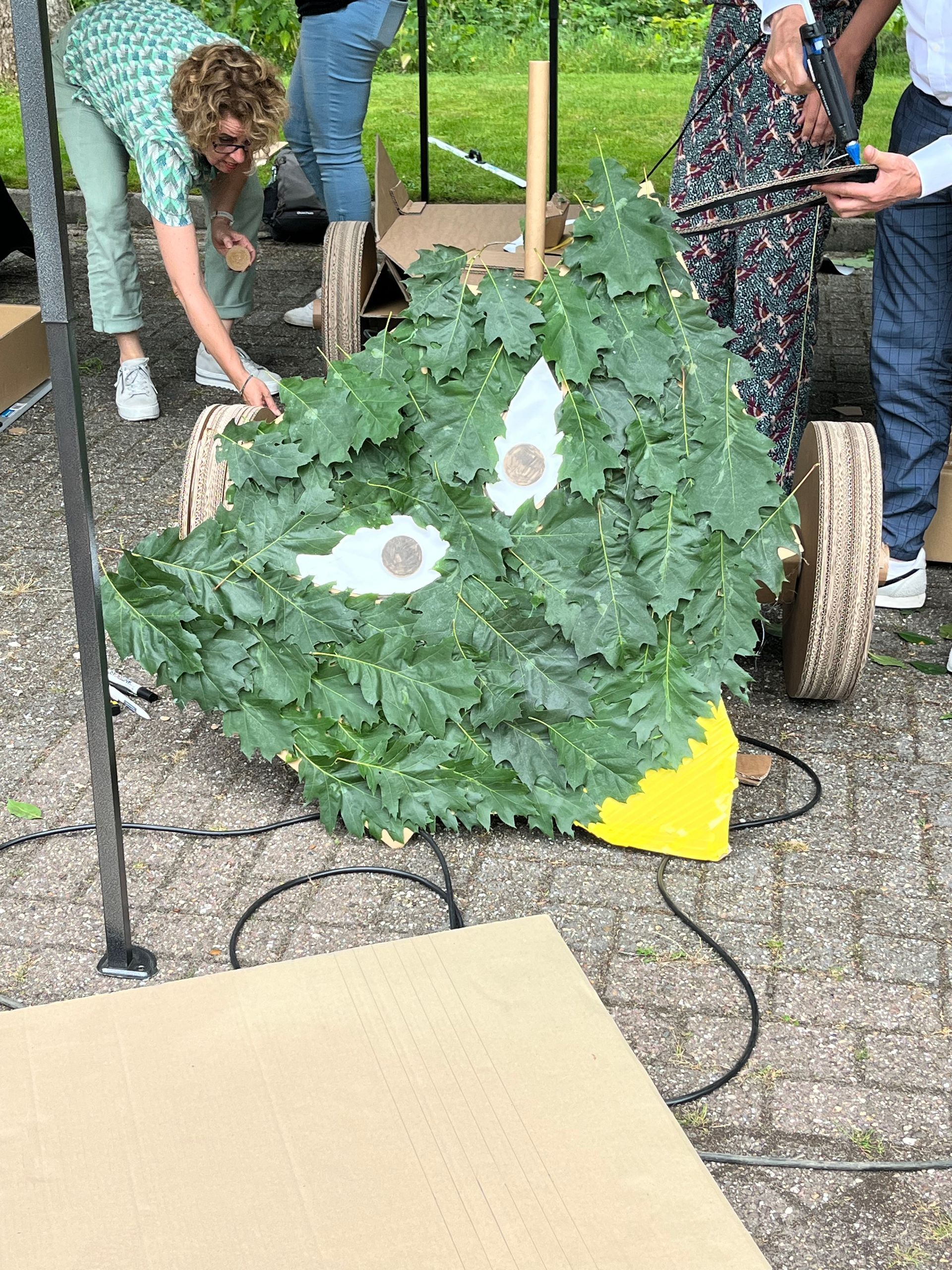 Een groep mensen werkt aan een sculptuur gemaakt van bladeren.