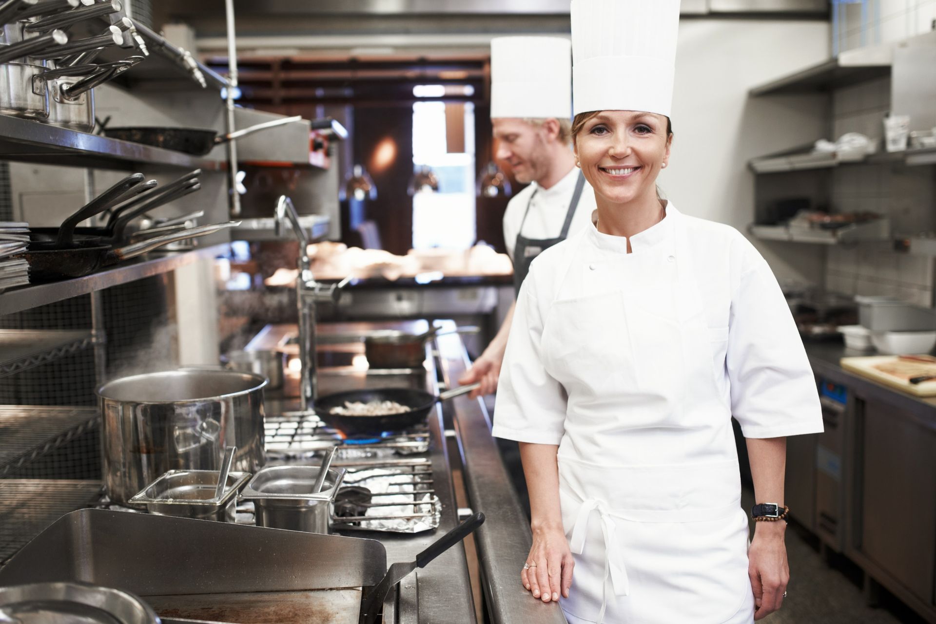 A woman in a chef 's uniform is standing in a kitchen.