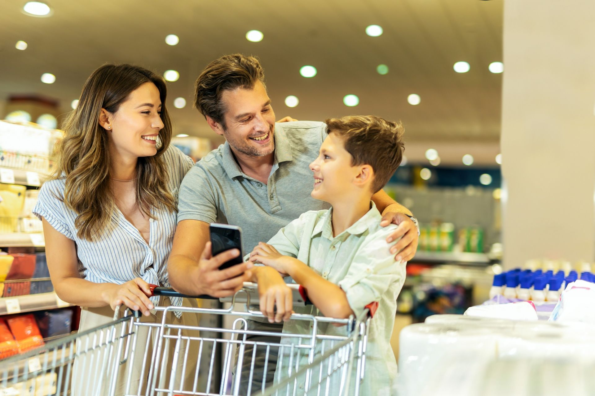 A family is shopping in a supermarket and looking at a cell phone.