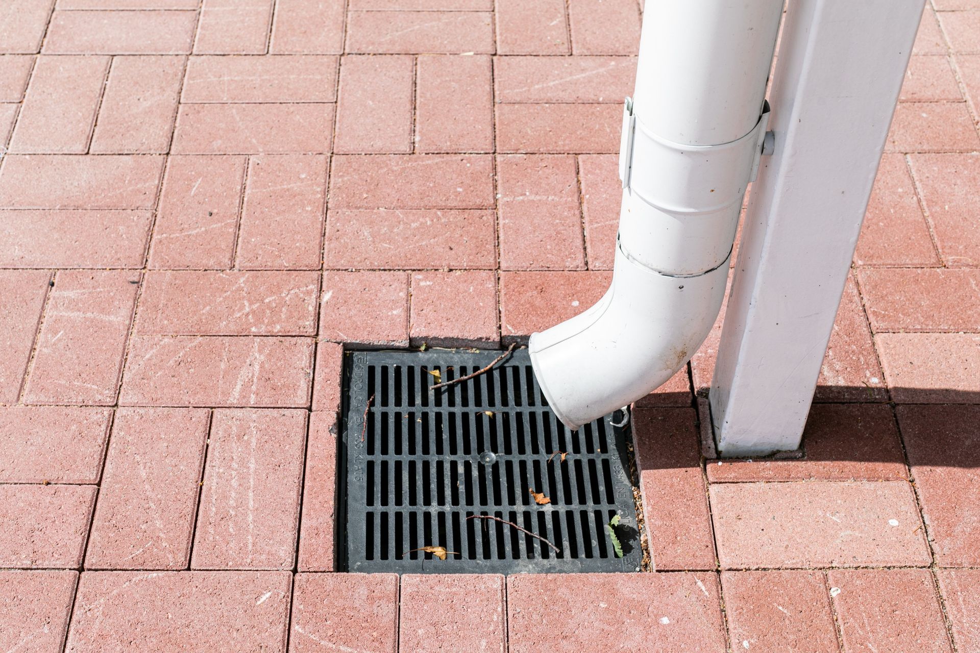 A white pipe is coming out of a drain on a brick sidewalk.