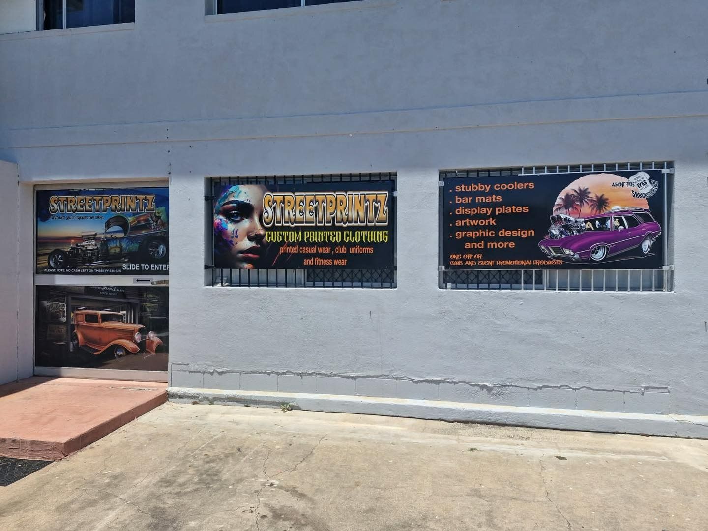 Exterior of business with three large signs and a door featuring vintage cars — That Printed Vinyl Place in Heatley, QLD