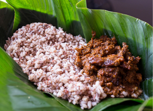 A close up of rice and meat on a banana leaf.