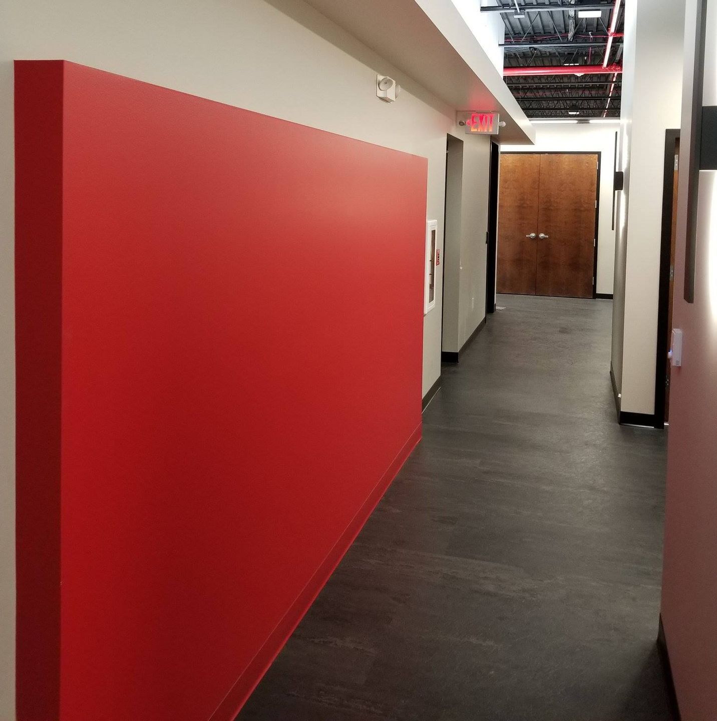 A hallway with a red wall and a red exit sign