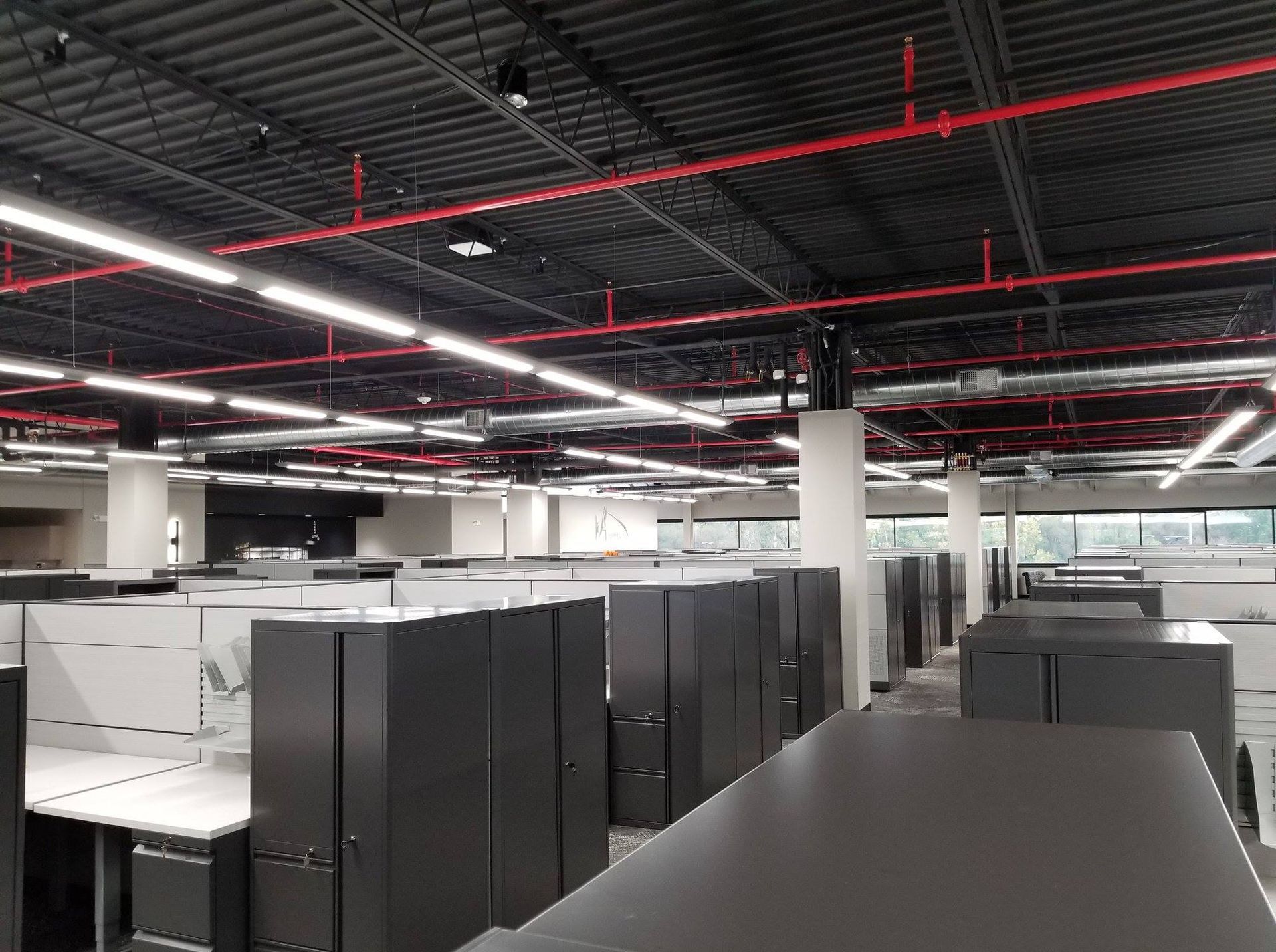 A large office with a lot of cubicles and fire sprinklers hanging from the ceiling.