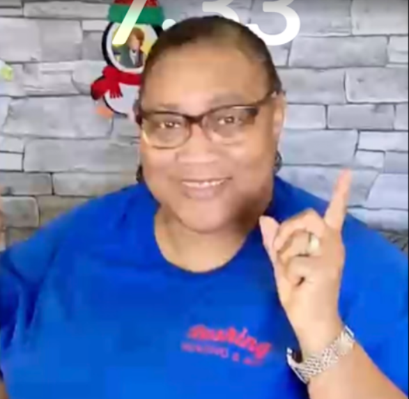 Woman in blue shirt pointing up, wearing glasses. Christmas decoration in background.