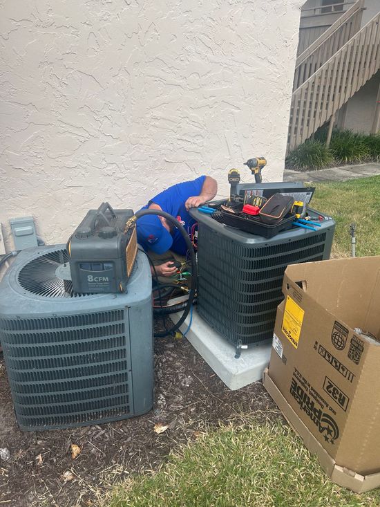 HVAC technician in blue shirt and cap working on an outdoor air conditioning unit.