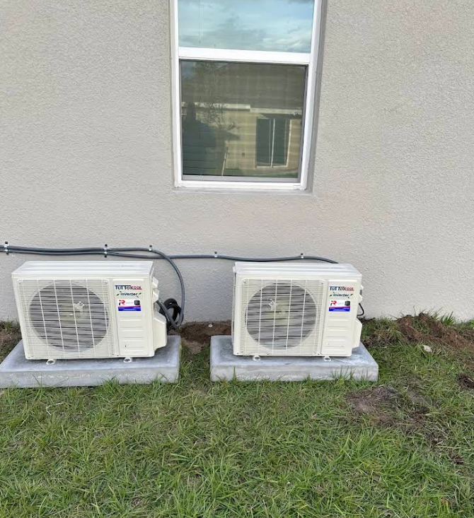 Two air conditioning units on concrete pads beside a building with a window.