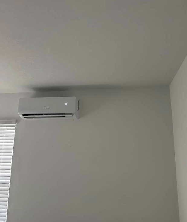 White wall-mounted air conditioner unit in a room with white walls and a window with blinds.