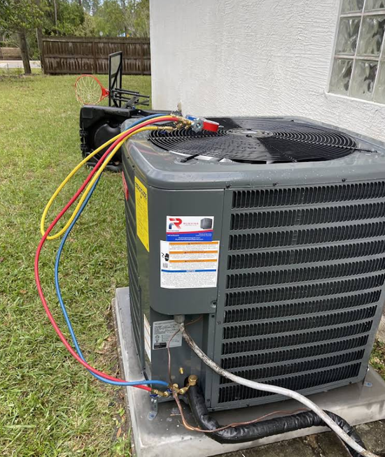 An air conditioning unit with hoses attached, outdoors, near a building.