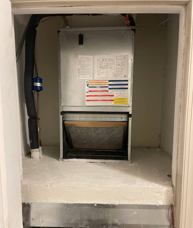Furnace unit in a closet. The unit is silver and rectangular, with air filter visible.