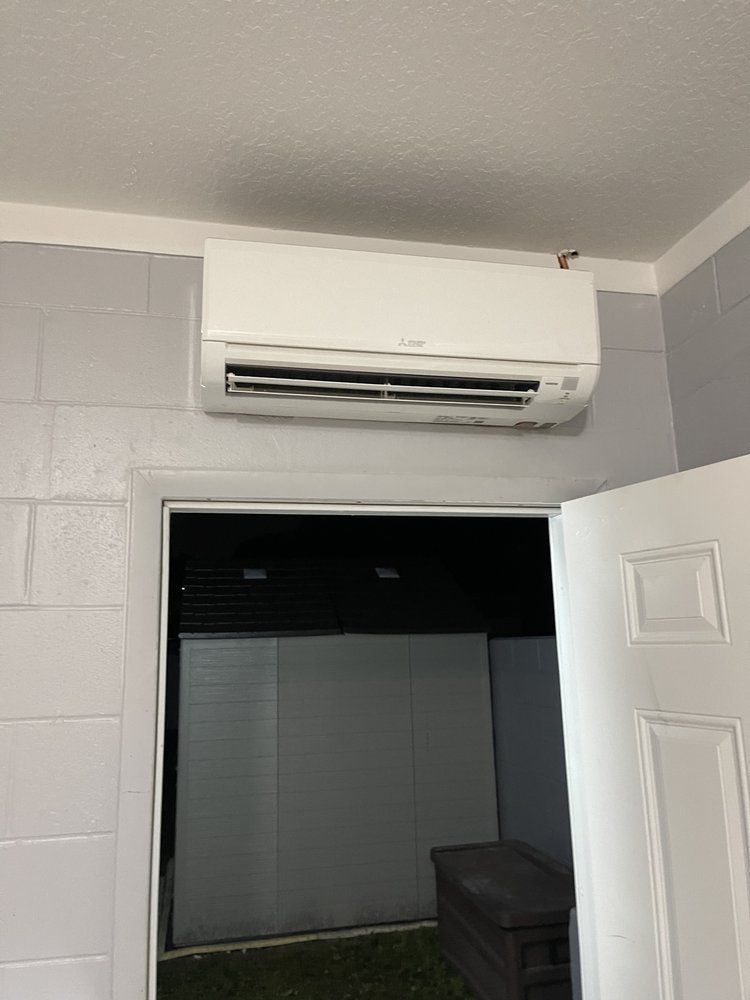 White air conditioning unit mounted on a gray wall above a doorway with an open white door.