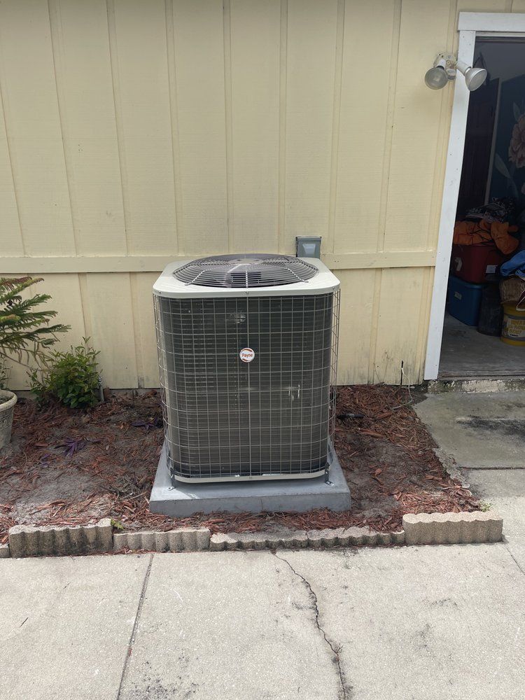 AC unit on a concrete pad, surrounded by mulch and decorative blocks, next to a beige building.