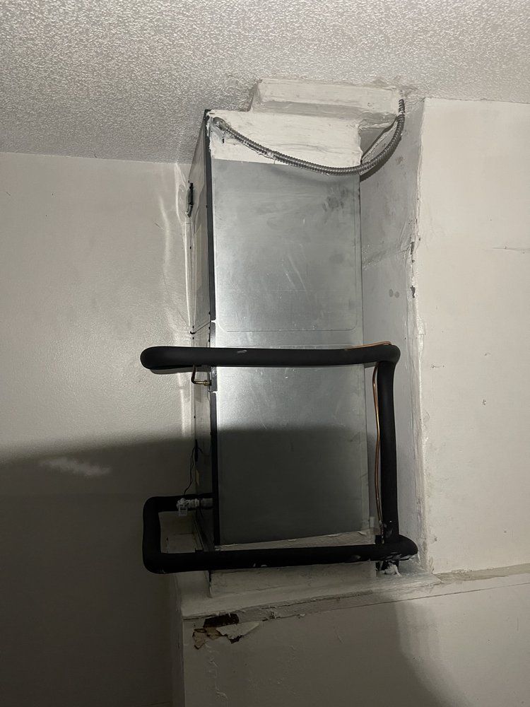 A rectangular metal ductwork opening in a white wall with black pipes and insulation.