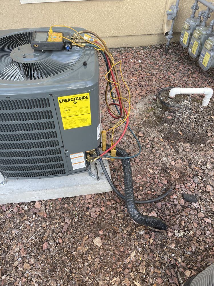 An air conditioning unit with gauges attached, outdoors on a gravel bed.