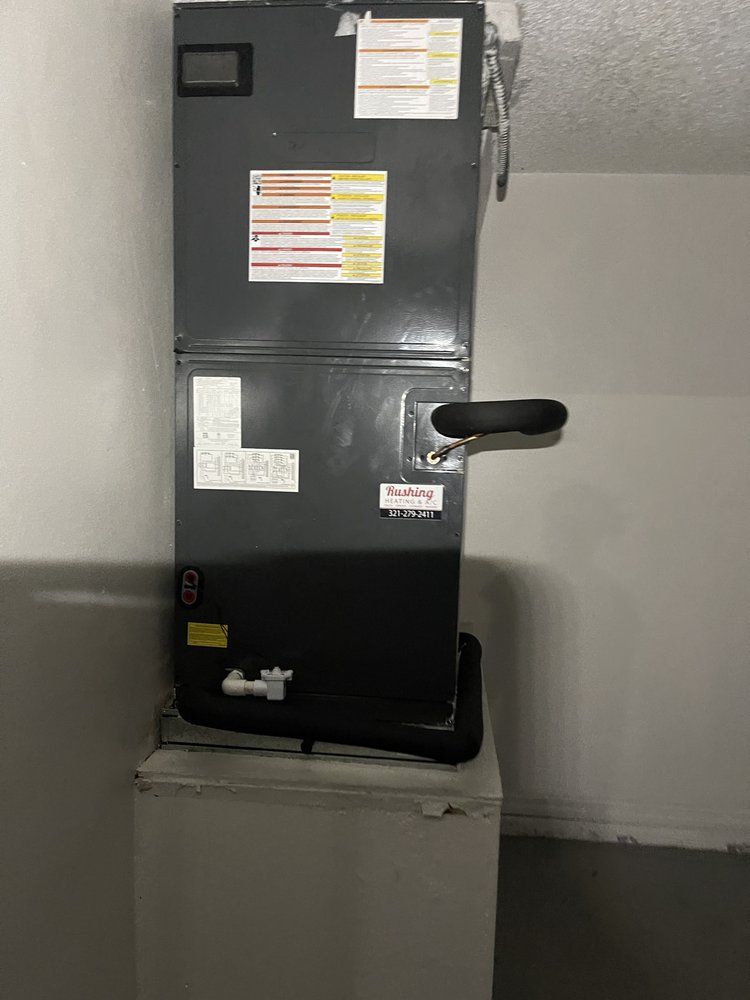 HVAC system, dark gray metal unit, attached to a white air handler, against a light gray wall.