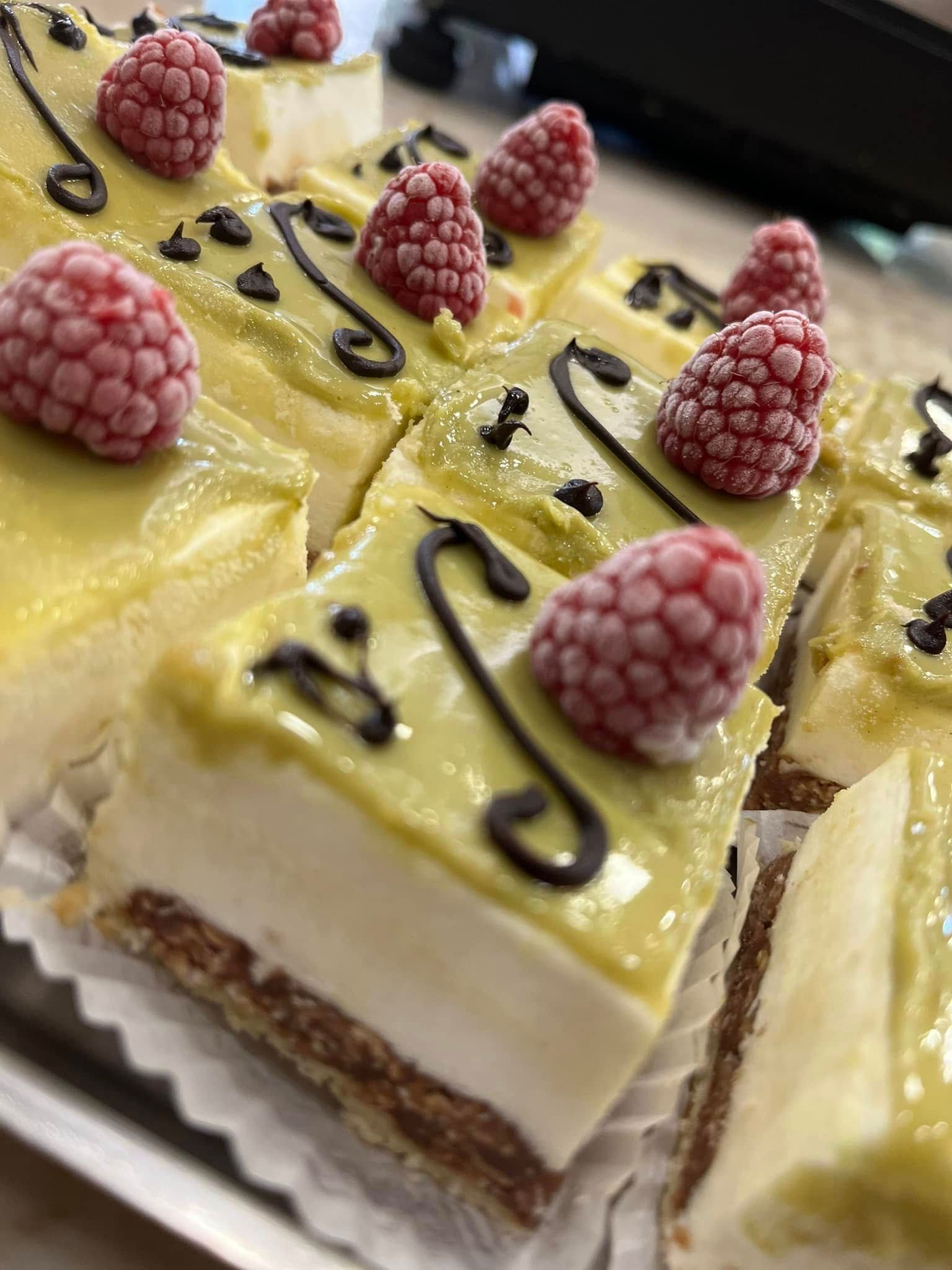 Fette di dessert a strati al lampone, guarnite con glassa gialla, salsa al cioccolato e lamponi freschi.