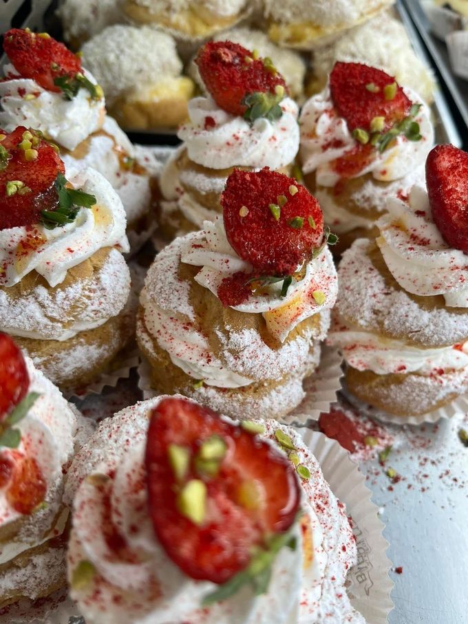 Mini pasticcini bianchi guarniti con panna montata, fragole, pistacchi e zucchero a velo su un vassoio