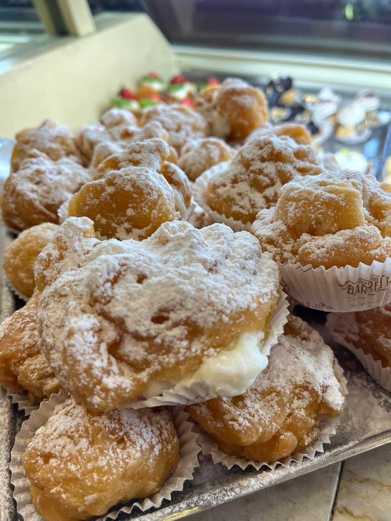 Vassoio di pasticcini ricoperti di zucchero a velo in pirottini di carta, impilati su un bancone espositivo.
