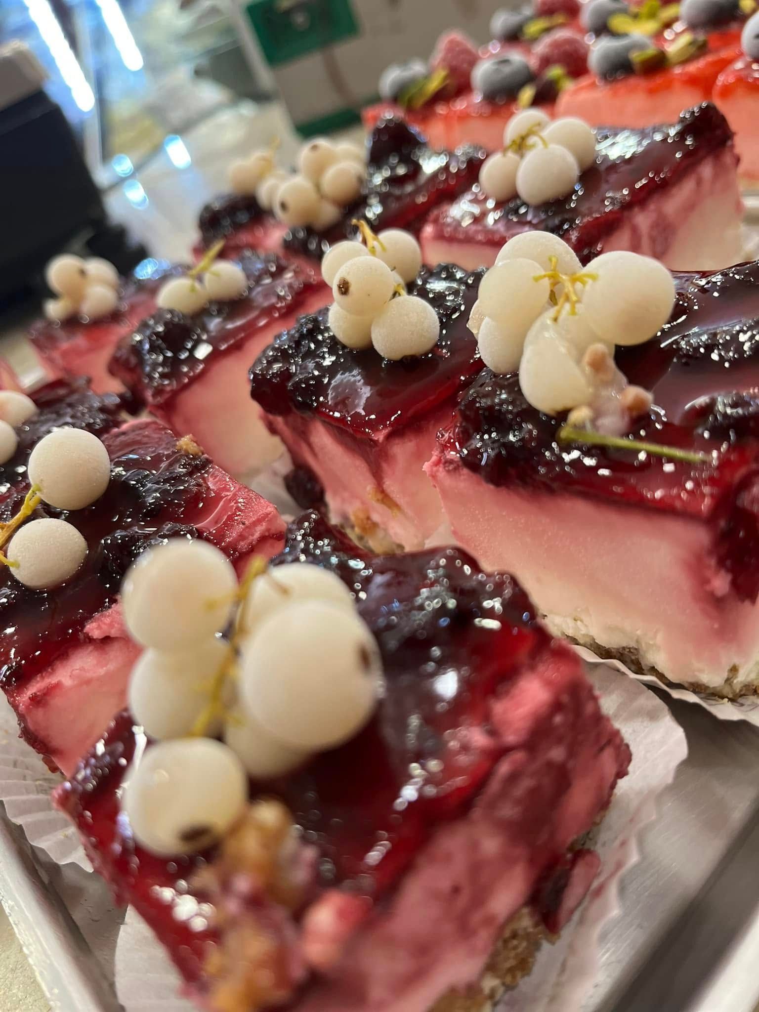 Quadratini da dessert glassati ai frutti di bosco e guarniti con perle di cioccolato bianco, disposti su un vassoio.