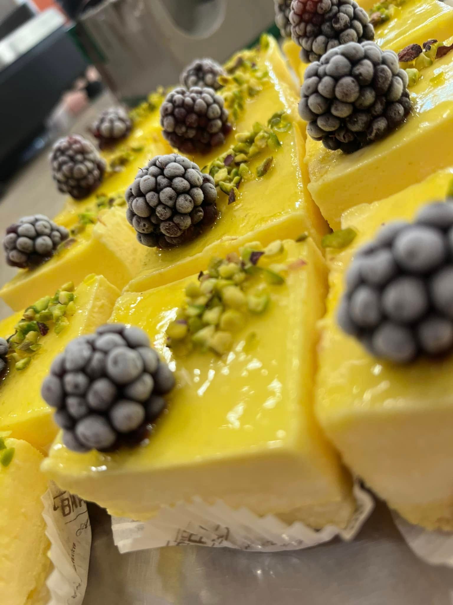 Quadratini da dessert gialli guarniti con more e pistacchi tritati su un vassoio