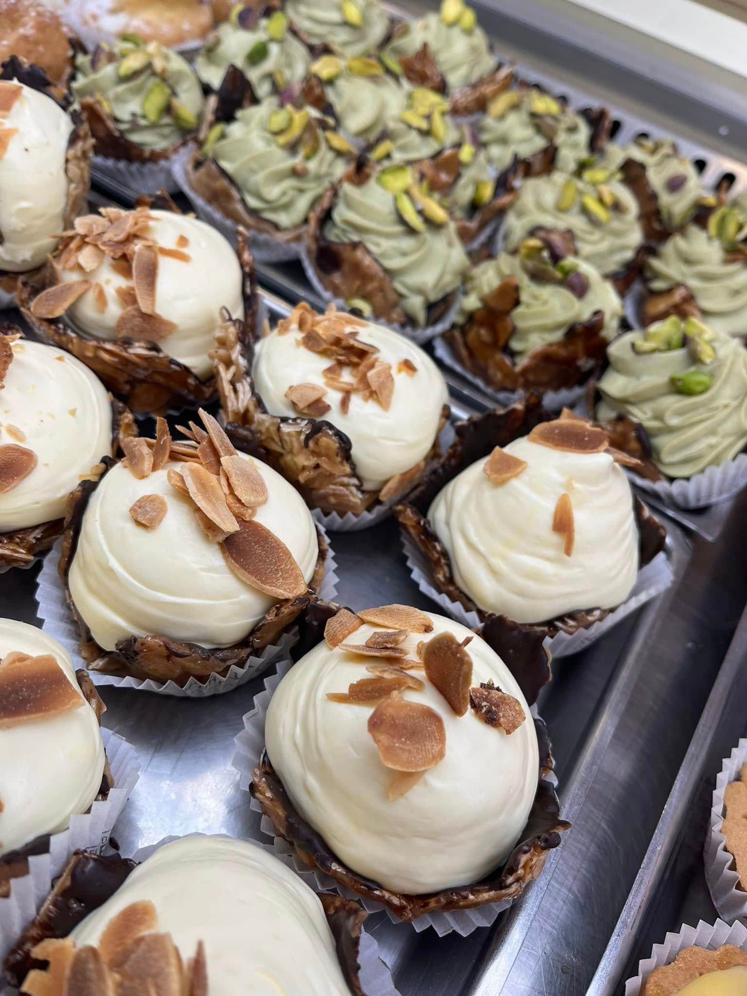 Vassoio di cupcake assortiti decorati con glassa bianca e al pistacchio e scaglie di mandorle.
