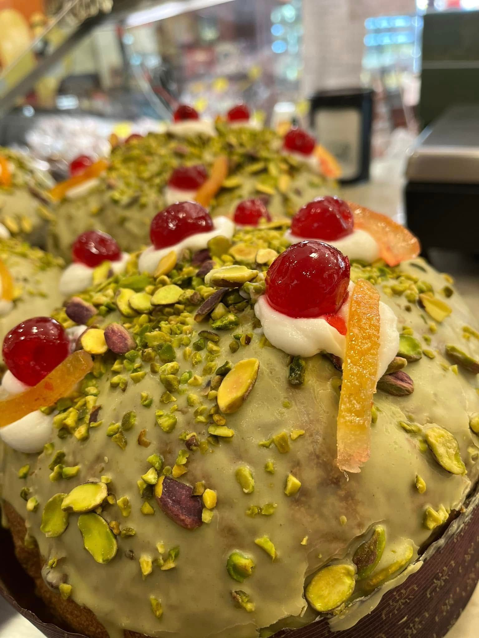 Torta da dessert con pistacchi, ciliegie e scorza d'arancia, servita su un piatto in un ambiente da caffetteria.